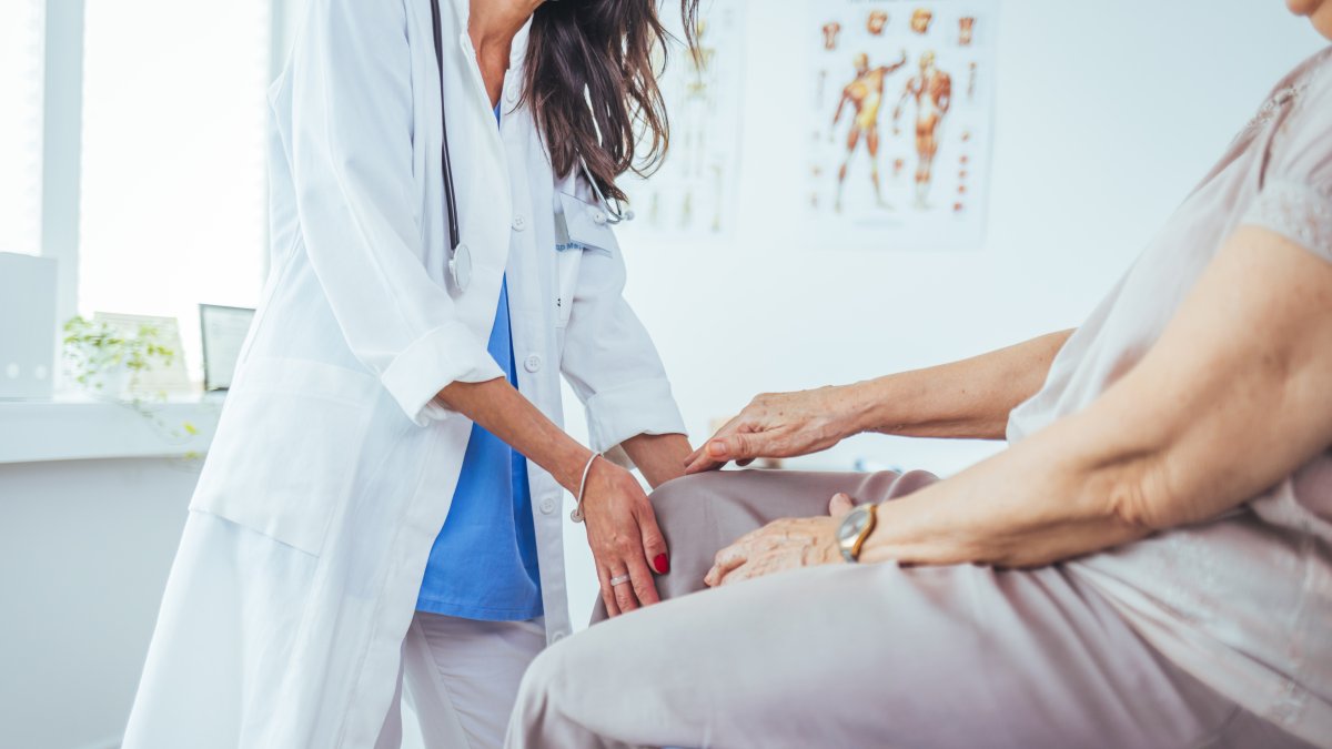 An elderly woman holds her knee, explaining her pain to a doctor. (Shutterstock Photo)