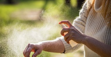 A person applies tick repellent spray before entering a wooded area to prevent bites. (Shutterstock Photo) 