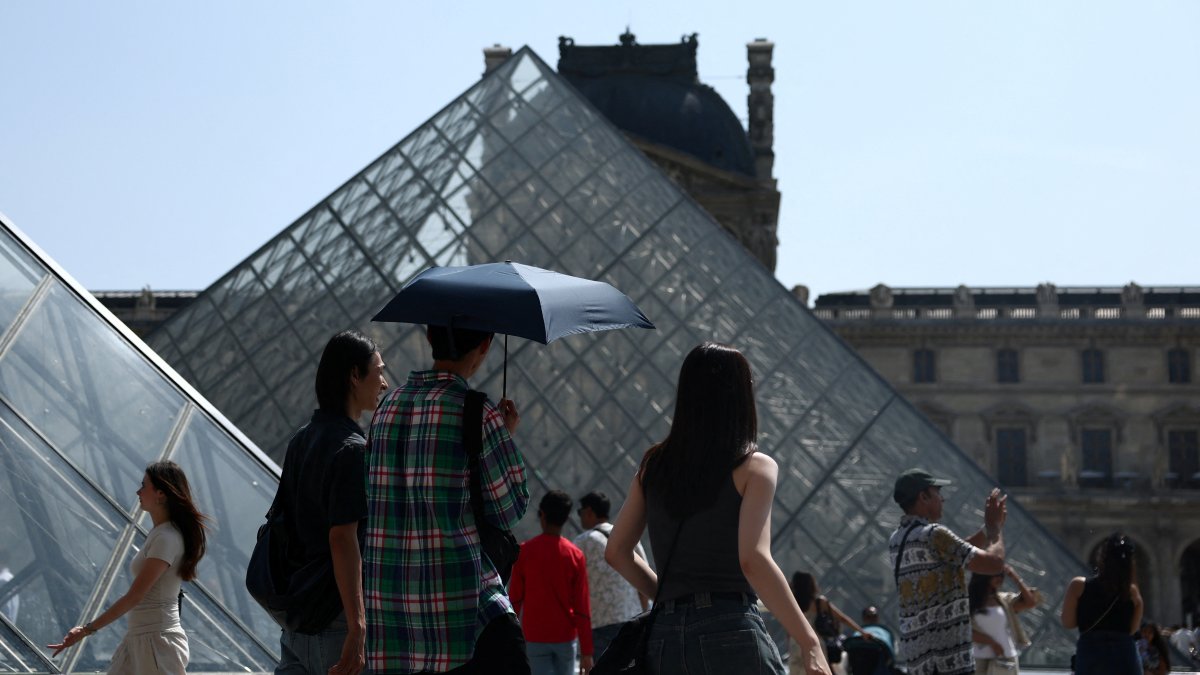 People holding an umbrella to protect themselves from the sun walk in front of the glass pyramid of the Louvre museum on a warm and sunny spring day, Paris, France, June 13, 2025. (Reuters Photo)