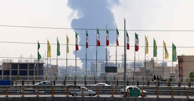Flags flutter along a bridge as a plume of heavy smoke and fire rises from an oil refinery in southern Tehran, Iran, June 15, 2025. (AFP Photo)