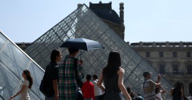 People holding an umbrella to protect themselves from the sun walk in front of the glass pyramid of the Louvre museum on a warm and sunny spring day, Paris, France, June 13, 2025. (Reuters Photo)