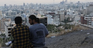 A man wears a U.S. veteran-themed shirt, that reads, &quot;United we stand&quot;, as smoke rises in the distance, following an Israeli attack on the IRIB building, the country&#039;s state broadcaster, in Tehran, Iran, June 16, 2025. (Reuters Photo)