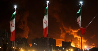 Iranian flags fly as fire and smoke from an Israeli attack on the Sharan Oil depot rise, Tehran, Iran, June 15, 2025. (Reuters Photo)