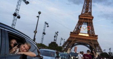 Passengers in the back of a taxi film themselves as they depart from the Eiffel Tower, decorated with the Olympic rings ahead of the 2024 Summer Olympics, Paris, France, July 17, 2024. (AP Photo)