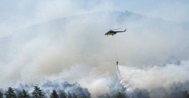 A helicopter conducts firefighting operations over the forest fires in Izmir’s Menderes district, supporting ground crews in controlling the blaze, Izmir, Türkiye,  June 30, 2025. (AA Photo) 