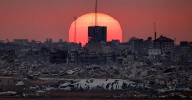 This picture taken from a position on the Israeli border with the Gaza Strip, shows the sun setting behind destroyed buildings in the Palestinian territory, July 1, 2025. (AFP Photo)