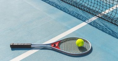 Tennis balls rest on a racket on a court. (Shutterstock Photo)