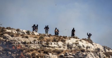 Masked Israeli settlers hurl rocks at Palestinians from hilltop in the village of Sinjil, in the occupied West Bank, July 4, 2025. (AFP Photo)