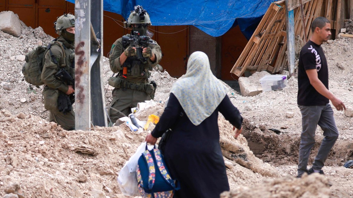 An Israeli soldier raises his rifle as Palestinians carry their belongings after being ordered to leave their homes in the Tulkarem refugee camp, occupied West Bank, Palestine, May 2, 2025. (AFP Photo)