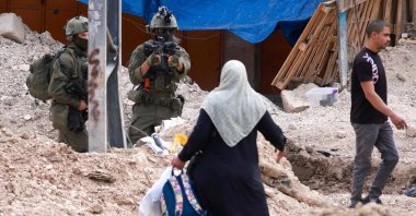 An Israeli soldier raises his rifle as Palestinians carry their belongings after being ordered to leave their homes in the Tulkarem refugee camp, occupied West Bank, Palestine, May 2, 2025. (AFP Photo)