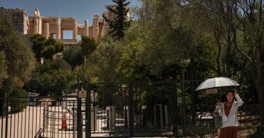 A tourist holds an umbrella as she stands in front of a closed gate to the Acropolis Hill in Athens, Greece, July 8, 2025. (AFP Photo)