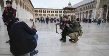 A boy poses for a photo with a masked Hayat Tahrir al-Sham (HTS) member in the courtyard of the Umayyad Mosque, Damascus, Syria, Dec. 10, 2024. (AP Photo)