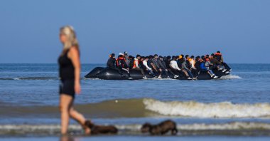 A tourist walks her dogs as migrants board a smuggler&#039;s boat in an attempt to cross the English Channel off the beach of Hardelot in Neufchatel-Hardelot, northern France, June 30, 2025. (AFP Photo)
