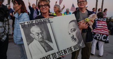 A protesting woman holds a sign that says &quot;Be the Change You want to see in the world&quot; with photos of Gandhi and Martin Luther King Jr. on the poster, in Santa Barbara, California, U.S., July 17, 2025. (Reuters Photo)