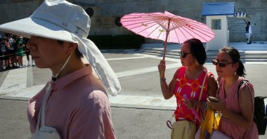 Tourists wear hats and use fans and umbrellas as they stroll in the city center during a heat wave, Athens, Greece, July 20, 2025. (EPA Photo)