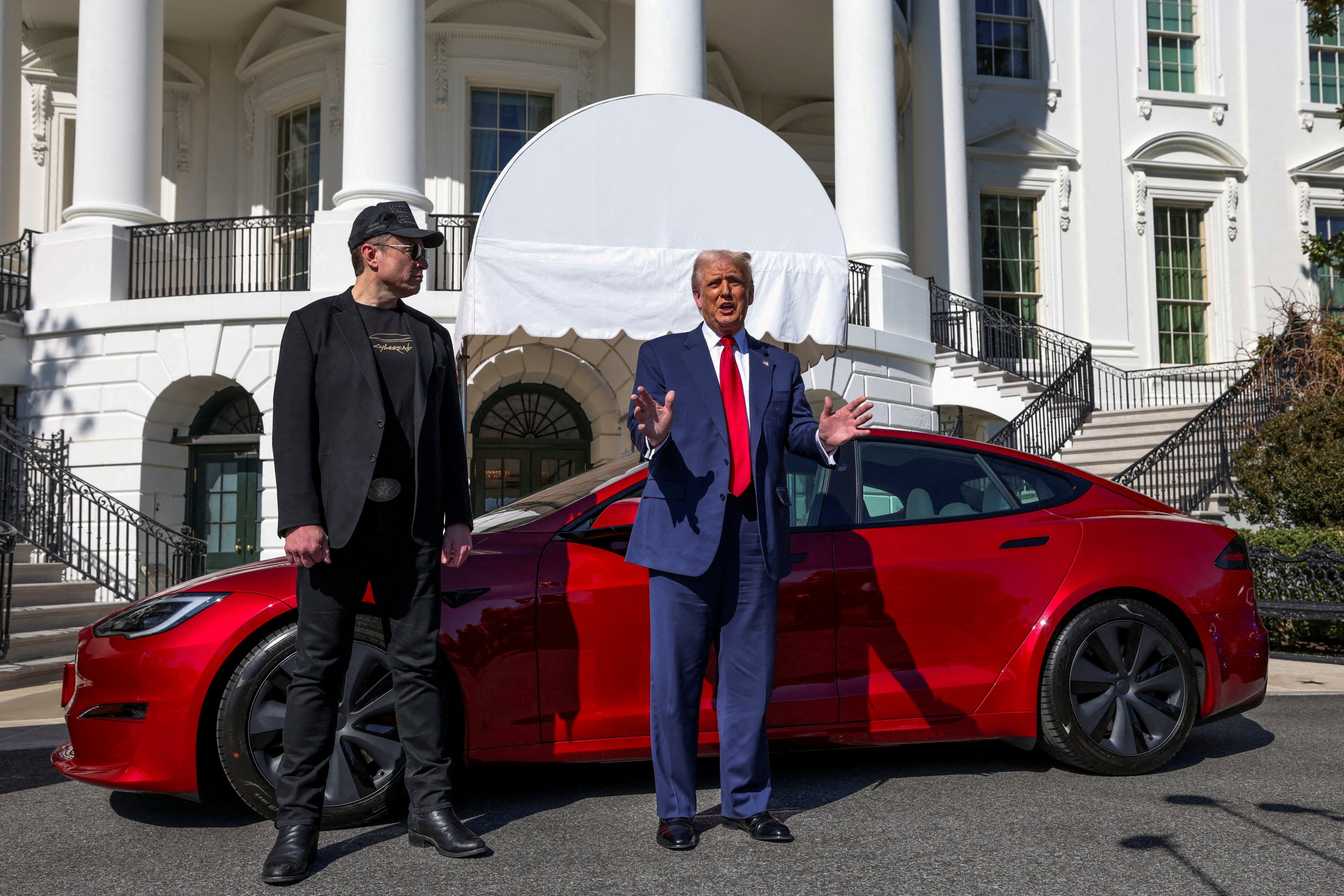 Elon Musk and Donald Trump standing beside a red Tesla Model S outside the White House.