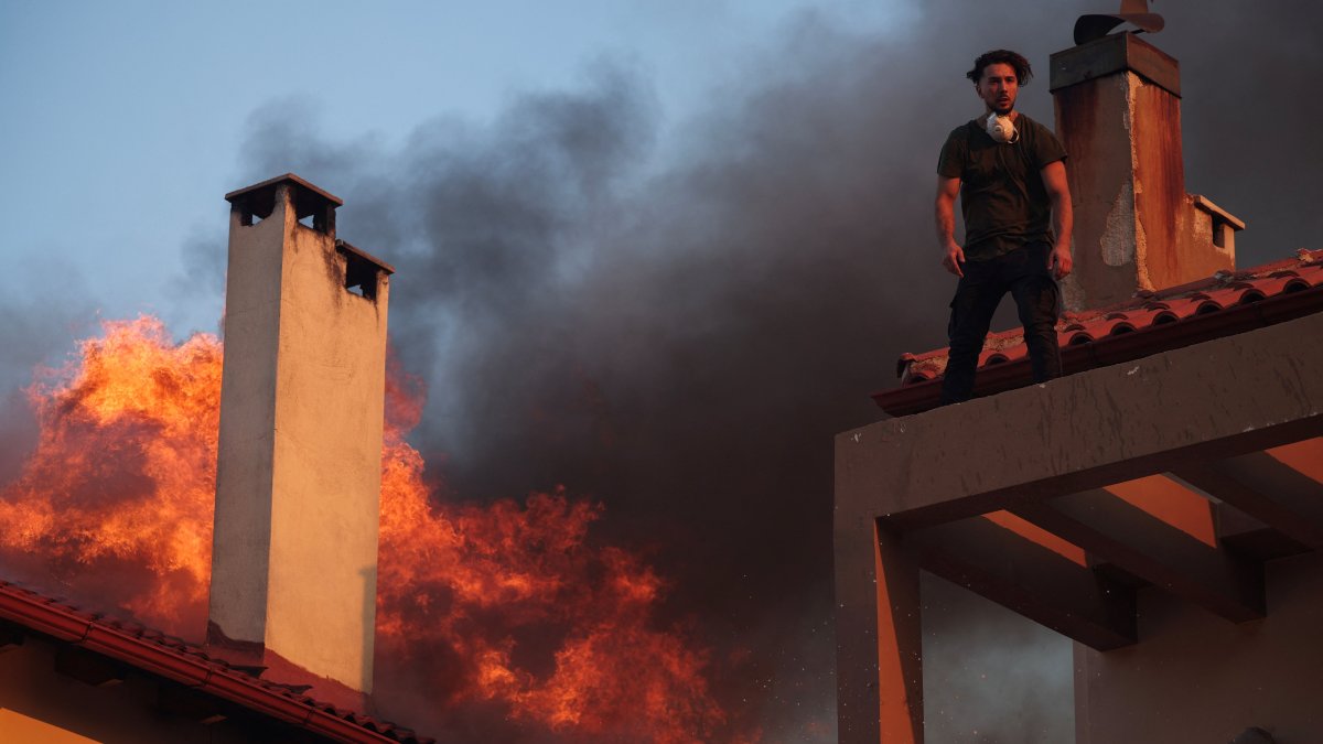 A local stands on a rooftop as flames rise from a burning house, while a wildfire burns in the village of Kryoneri, near Athens, Greece, July 26, 2025. (Reuters Photo)