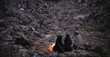 Members of a family keep warm next to a fire as they follow a rescue team searching for their relatives among destroyed buildings in Antakya, Türkiye, Feb. 15, 2023. (AP Photo)