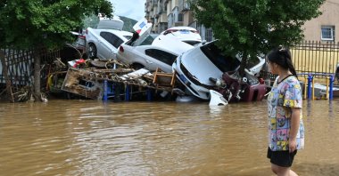 A woman walks past damaged cars in a flooded neighborhood in Miyun district, northern Beijing, July 29, 2025. (AFP Photo)