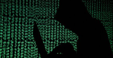 A hooded man holds a laptop computer as cyber code is projected on him in this illustration picture, May 13, 2017. (Reuters Photo)
