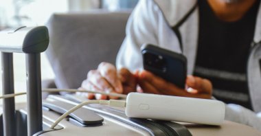 A man waits in an airport lounge, charging his phone using a power bank before departure. (Shutterstock Photo)