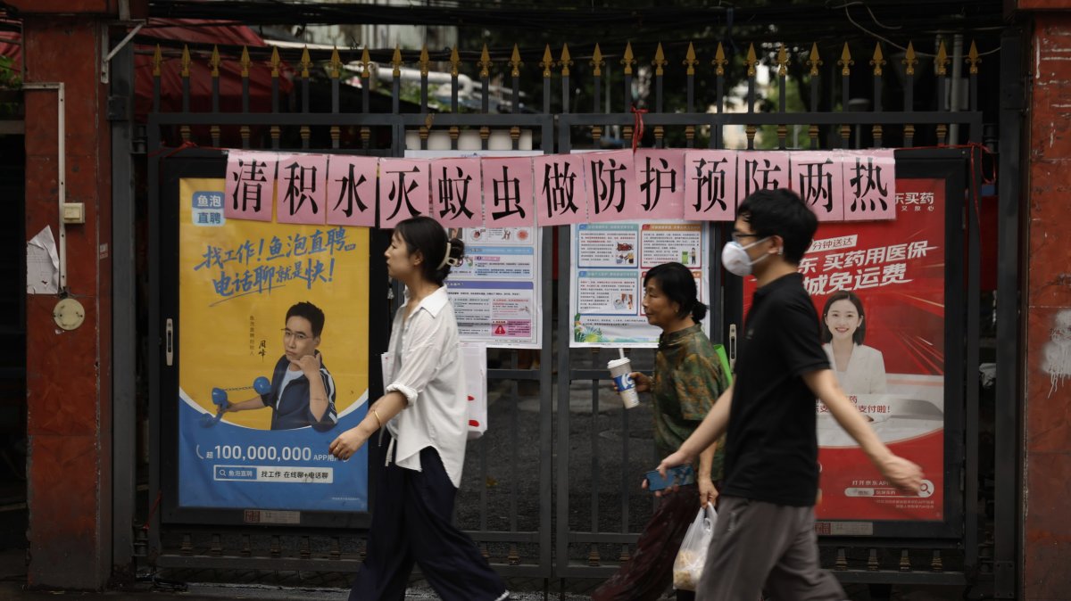 Residents walk past a residential entrance gate displaying a slogan urging mosquito control, Guangzhou, China, Aug. 6, 2025. (AP Photo)