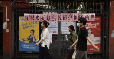 Residents walk past a residential entrance gate displaying a slogan urging mosquito control, Guangzhou, China, Aug. 6, 2025. (AP Photo)