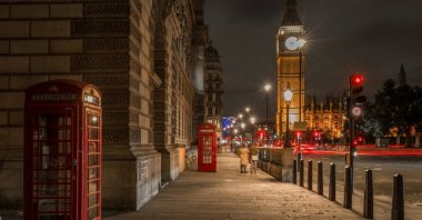 Red telephone boxes in London illuminated by moonlight and city lights, with Big Ben visible in the background. (Shutterstock Photo)