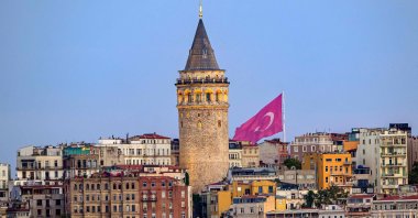 A Turkish flag is seen behind the Galata Tower at sunrise in Istanbul, Türkiye, Aug. 9, 2025. (AFP Photo)