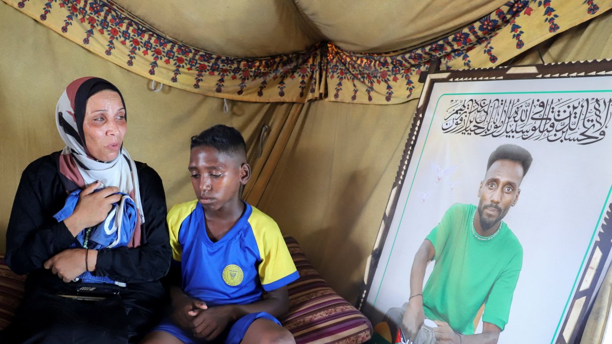 Doaa, the widow of late football player Suleiman Al-Obeid, known as the "Palestinian Pele," who was killed by an Israeli strike targeting people waiting for humanitarian aid, looks at his picture while holding his shorts, as her son sits beside her inside their tent, Gaza City, Palestine, Aug. 9, 2025. (Reuters Photo)