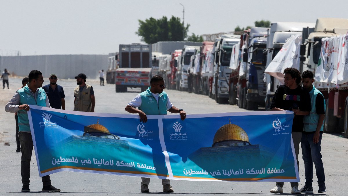 People hold a banner that reads "The distance to help our people in Palestine" as trucks carrying humanitarian aid line up near the Rafah border crossing between Egypt and the Gaza Strip, in Rafah, Egypt, Aug.6, 2025. (Reuters Photo)