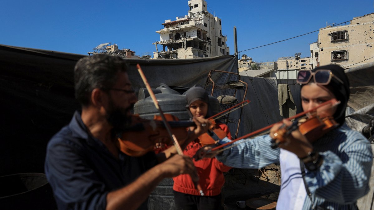 Music instructor Ahmed Abu Amsha (L) of the Edward Said National Conservatory of Music, conducts a lesson for Palestinian girls as a building damaged in the Israeli offensive appears in the background, Gaza City, Palestine, Aug. 5, 2025. (Reuters Photo)
