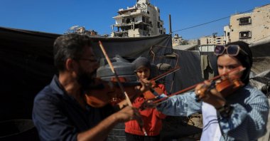 Music instructor Ahmed Abu Amsha (L) of the Edward Said National Conservatory of Music, conducts a lesson for Palestinian girls as a building damaged in the Israeli offensive appears in the background, Gaza City, Palestine, Aug. 5, 2025. (Reuters Photo)