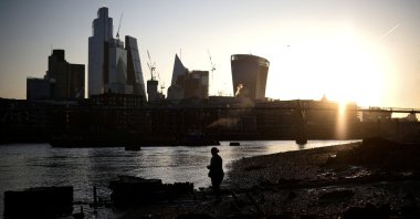 A person stands on the bank of the River Thames during sunrise, with the City of London financial district in the background, in London, U.K., April 4, 2023. (Reuters Photo)
