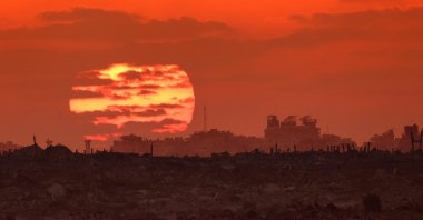 In this picture taken from a position on the Israeli border with the Gaza Strip, the sun sets behind destroyed buildings in the Palestinian territory, Aug. 7, 2025. (AFP Photo)
