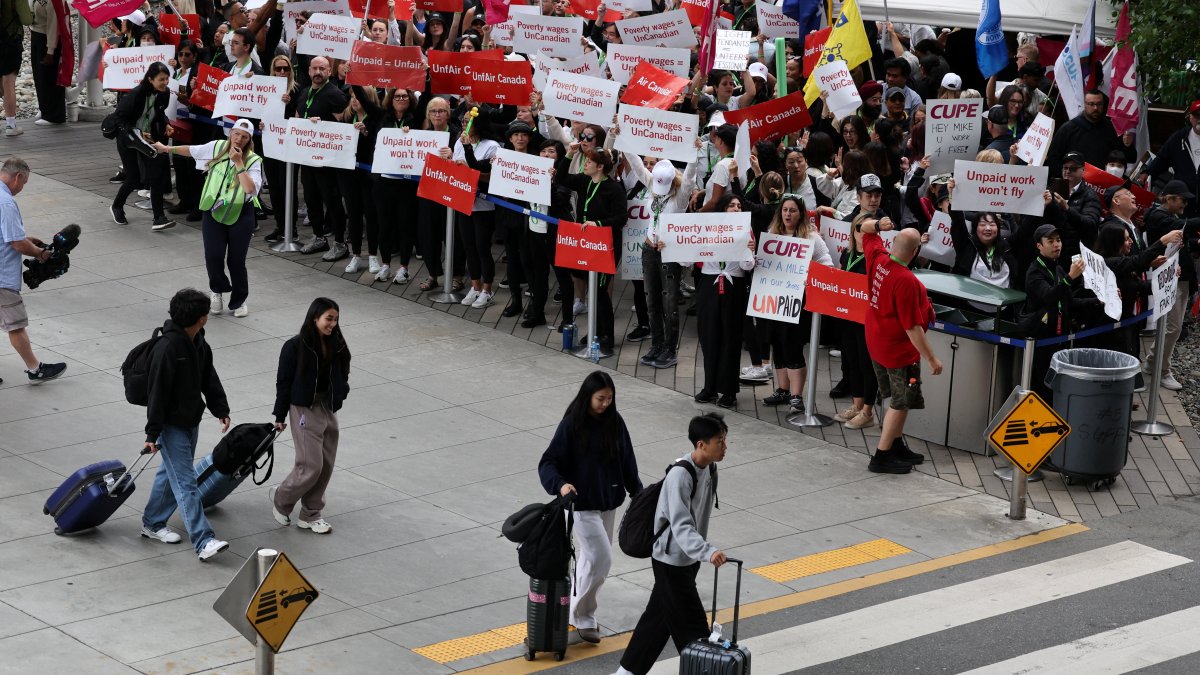 Passengers walk in front of demonstrators holding placards as Air Canada flight attendants said they will remain on strike and challenge a return-to-work defying a government decision to force them back, Vancouver International Airport, British Columbia, Canada, Aug. 17, 2025. (Reuters Photo)