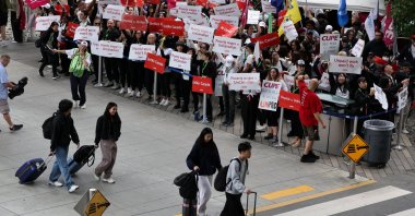 Passengers walk in front of demonstrators holding placards as Air Canada flight attendants said they will remain on strike and challenge a return-to-work defying a government decision to force them back, Vancouver International Airport, British Columbia, Canada, Aug. 17, 2025. (Reuters Photo)