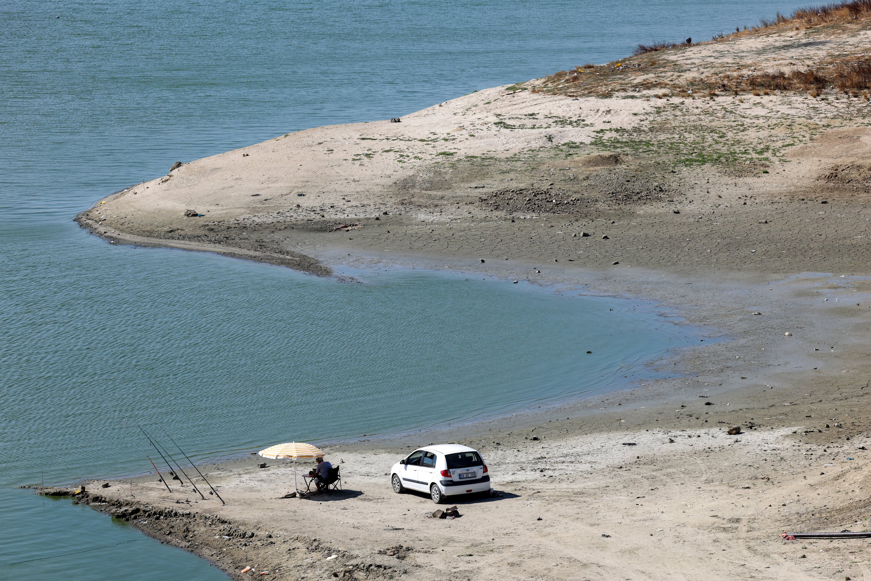 A person sits under an umbrella with fishing rods set up near the receding shoreline of Türkmenli Dam, as drought conditions continue to affect water levels, in Marmaraereğlisi, northwestern Tekirdağ province, Türkiye, Aug. 11, 2025. (Reuters Photo)