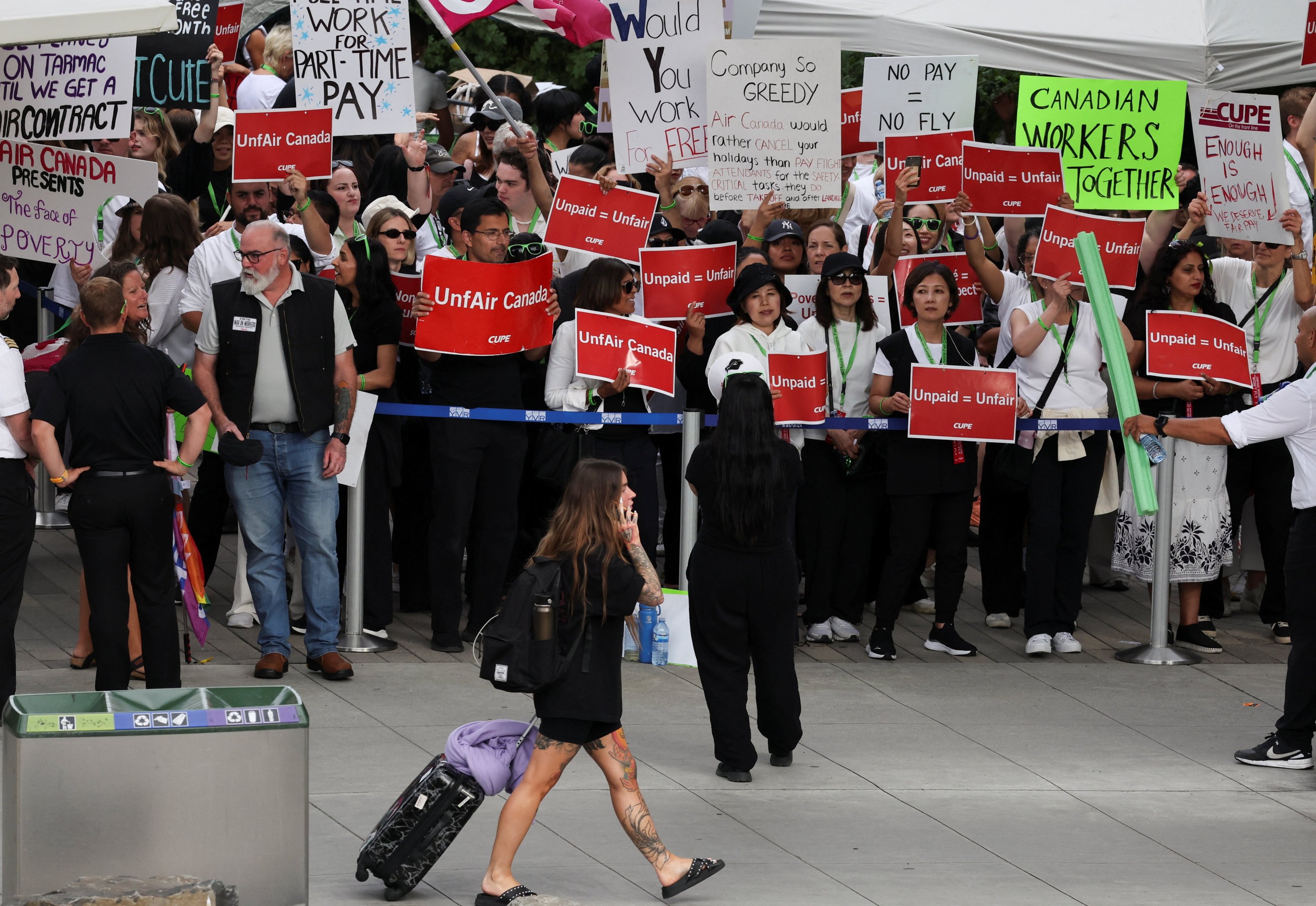 A passenger walks as striking Air Canada flight attendants hold placards at Vancouver International Airport in Richmond, British Columbia, Canada, Aug. 18, 2025. (Reuters Photo)