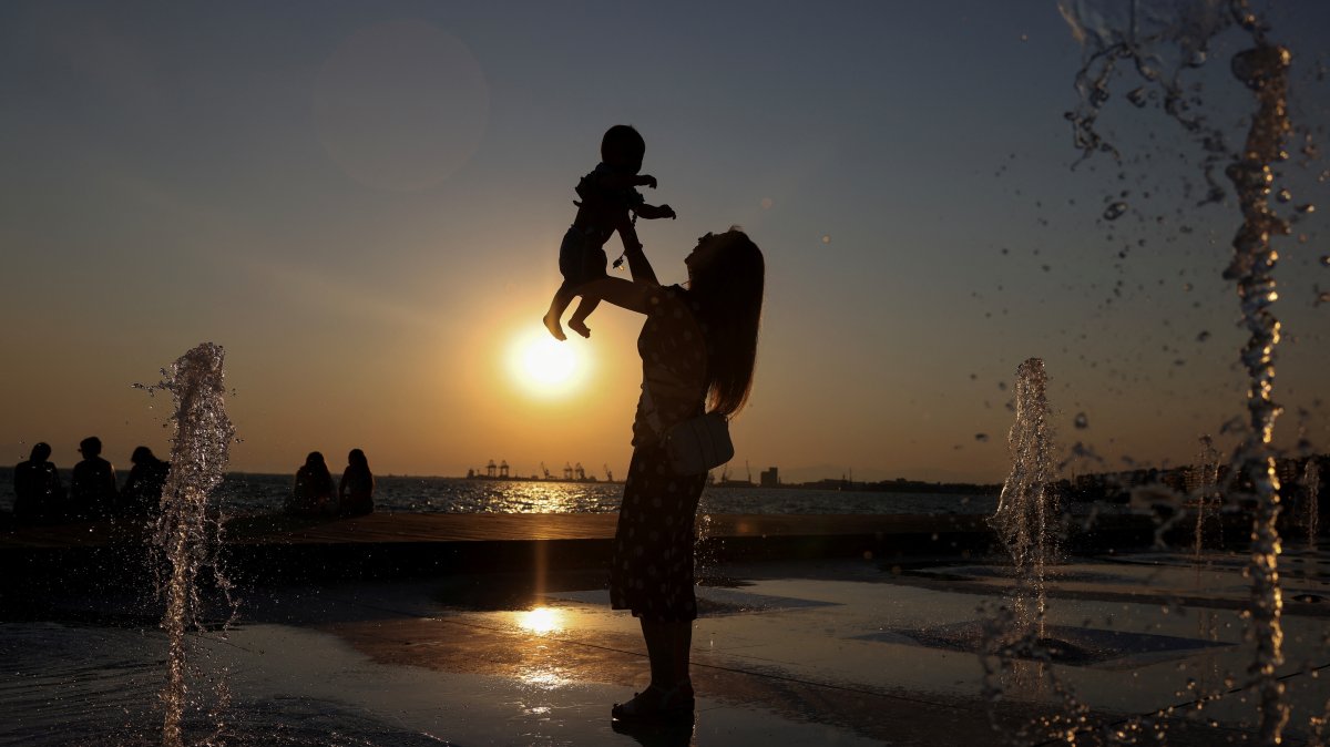 A woman lifts a baby while standing in a fountain during a hot day, Thessaloniki, Greece, July 21, 2025. (Reuters Photo)