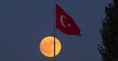 A full moon appears behind a waving Turkish flag, Karaman, Türkiye, Aug. 8, 2025. (AA Photo)
