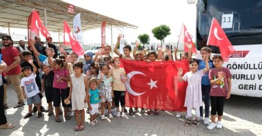 A group of Syrian children waves Turkish flags before boarding a bus at a voluntary return coordination center, en route to the border, in southern Adana province, Türkiye, Aug. 19, 2025. (IHA Photo) 