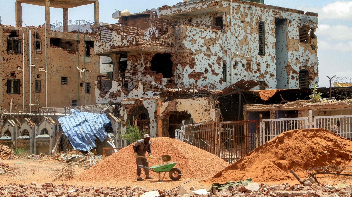 A worker shovels pebbles from a mound into a wheelbarrow near heavily-damaged buildings at a site in Khartoum, Sudan, July 30, 2025. (AFP Photo)