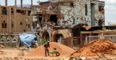 A worker shovels pebbles from a mound into a wheelbarrow near heavily-damaged buildings at a site in Khartoum, Sudan, July 30, 2025. (AFP Photo)