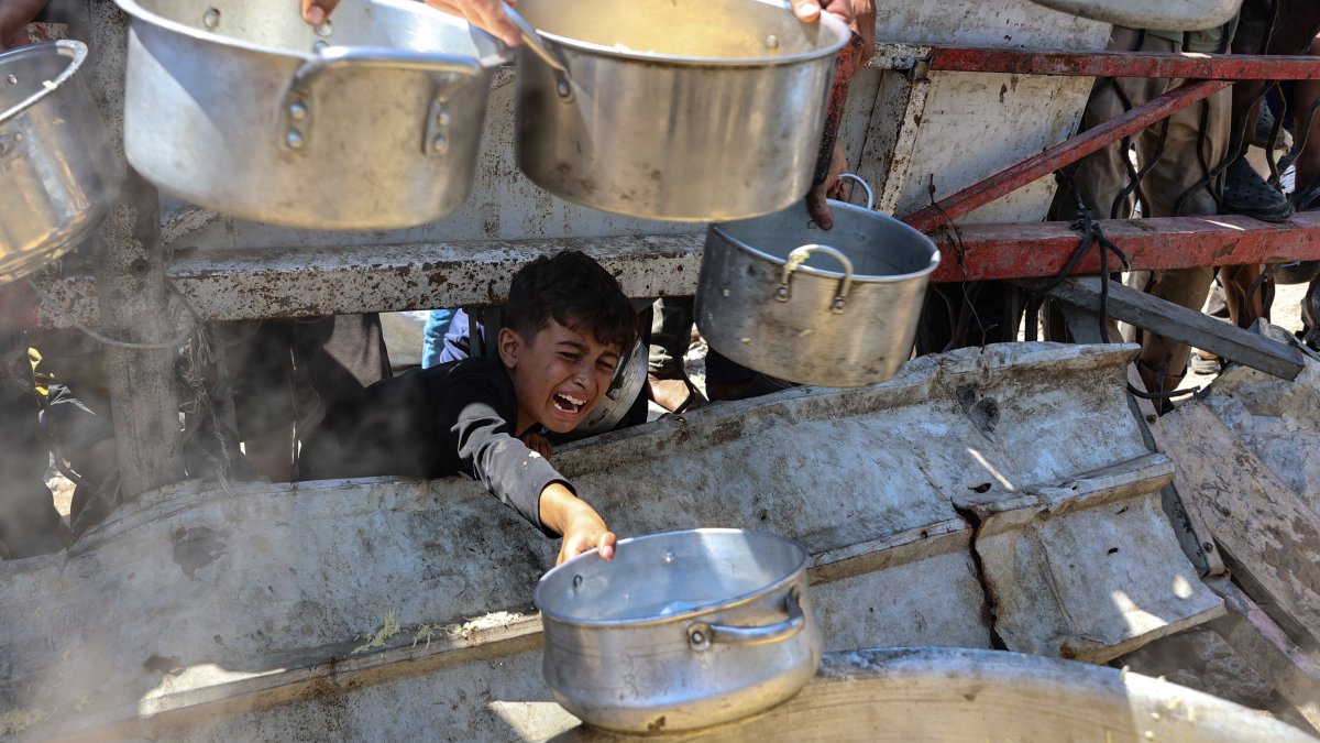 A Palestinian boy extends an empty pot in front of a charity kitchen to receive cooked rice, Gaza City, Palestine, Aug. 23, 2025. (AFP Photo)