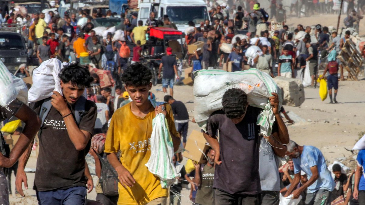 People walk with bags of humanitarian aid they received at a distribution centre run by the Gaza Humanitarian Foundation (GHF), as they cross the so-called &quot;Netzarim corridor&quot; in the central Gaza Strip, Aug. 22, 2025. (AFP Photo)