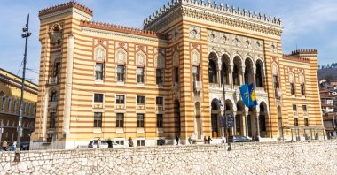The Sarajevo City Hall, also known as Vijecnica, on a sunny day, with the Bosnian flag flying at its entrance, Sarajevo, Bosnia-Herzegovina, March 8, 2025. (Shutterstock Photo)