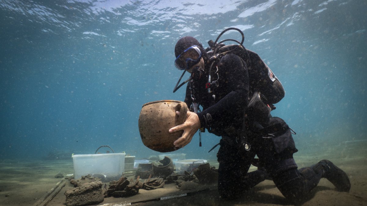 A diver from the excavation team holds an artifact found at the Ottoman shipwreck, Muğla, southwestern Türkiye, Aug. 24, 2025. (AA Photo)