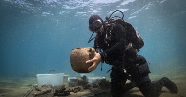 A diver from the excavation team holds an artifact found at the Ottoman shipwreck, Muğla, southwestern Türkiye, Aug. 24, 2025. (AA Photo)