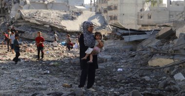 A Palestinian woman carries a child, as they inspect the site of an overnight Israeli strike on a house in Gaza City, Palestine, Aug. 26, 2025. (Reuters Photo)
